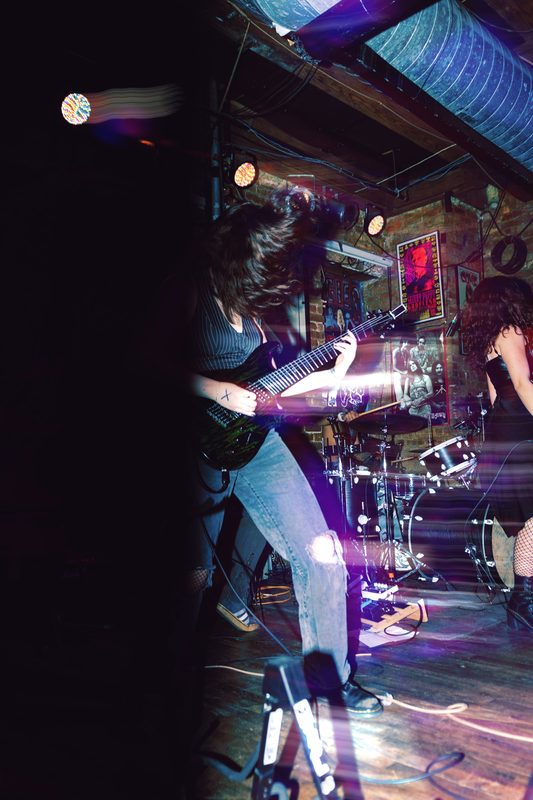 Kylee playing a seven-string guitar on stage, streaked with purple motion blur