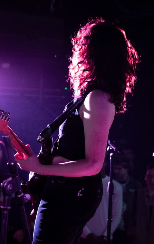 Kylee in profile, hair backlit pink, playing guitar on stage