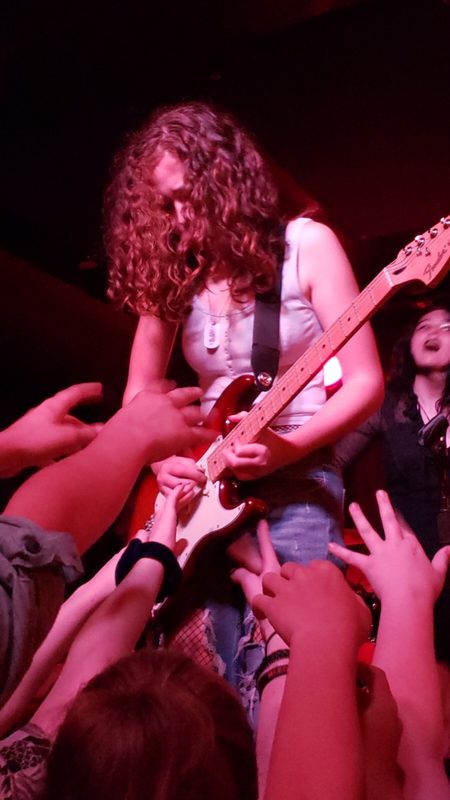 Kylee on stage under red light, crowd reaching up